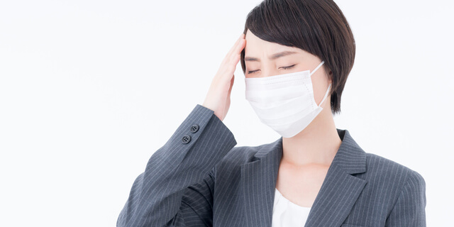 頭を押さえるマスクの女性